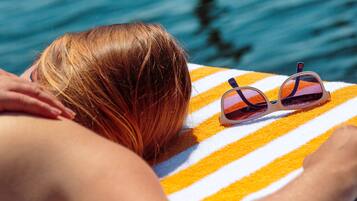 A person lying on a striped towel by a body of water.