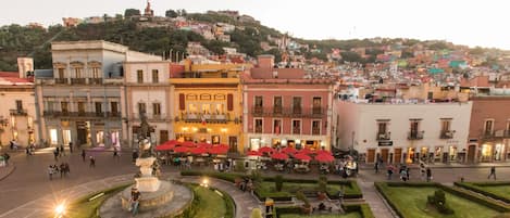 Una plaza con una estatua en el centro, rodeada de edificios con terrazas y una fuente.