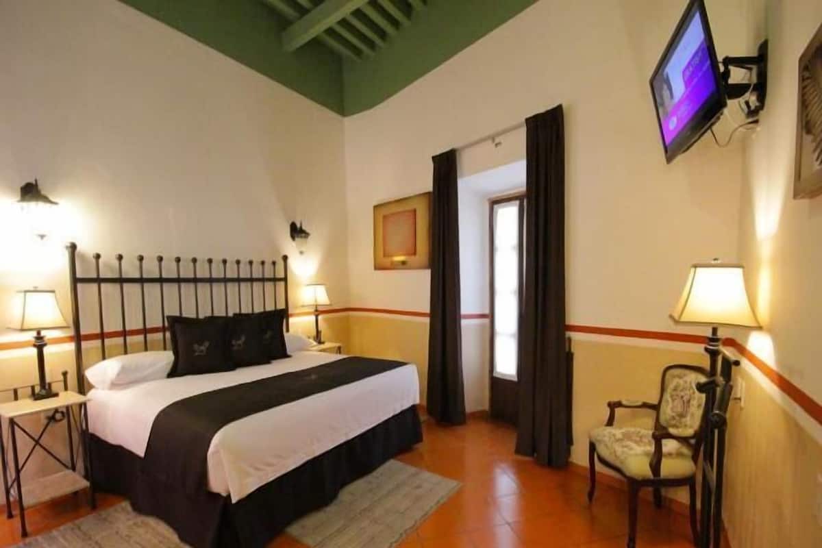 Une chambre d’hôtel comprenant un lit, deux lampes de chevet, une télévision, une chaise et une porte donnant sur une autre pièce.