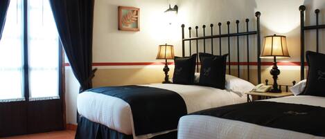 A hotel room with two beds, a nightstand with a lamp, a telephone, and a painting on the wall.
