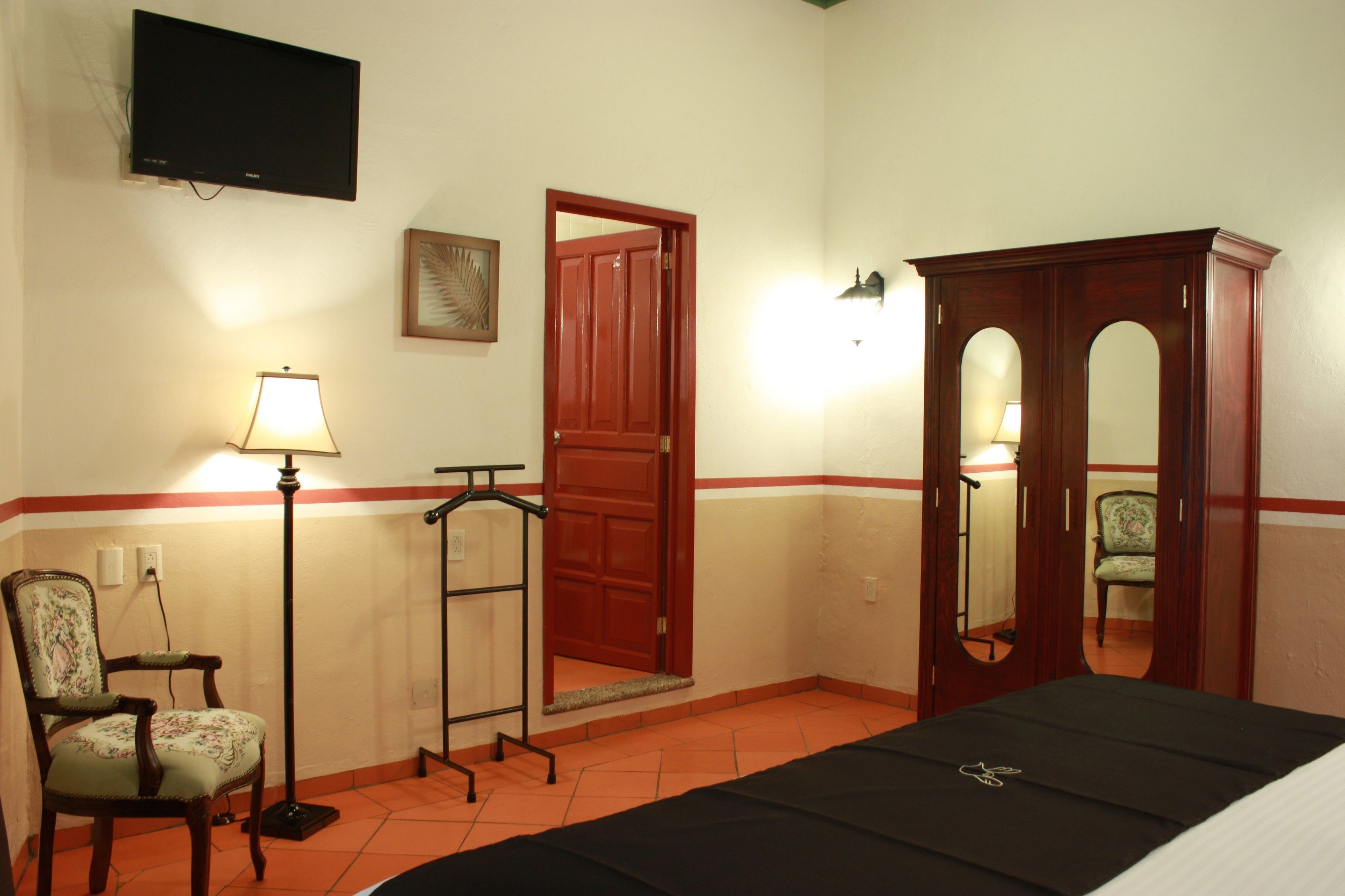 Una habitación de hotel con una cama, una silla, un escritorio, un armario, un televisor y una puerta.