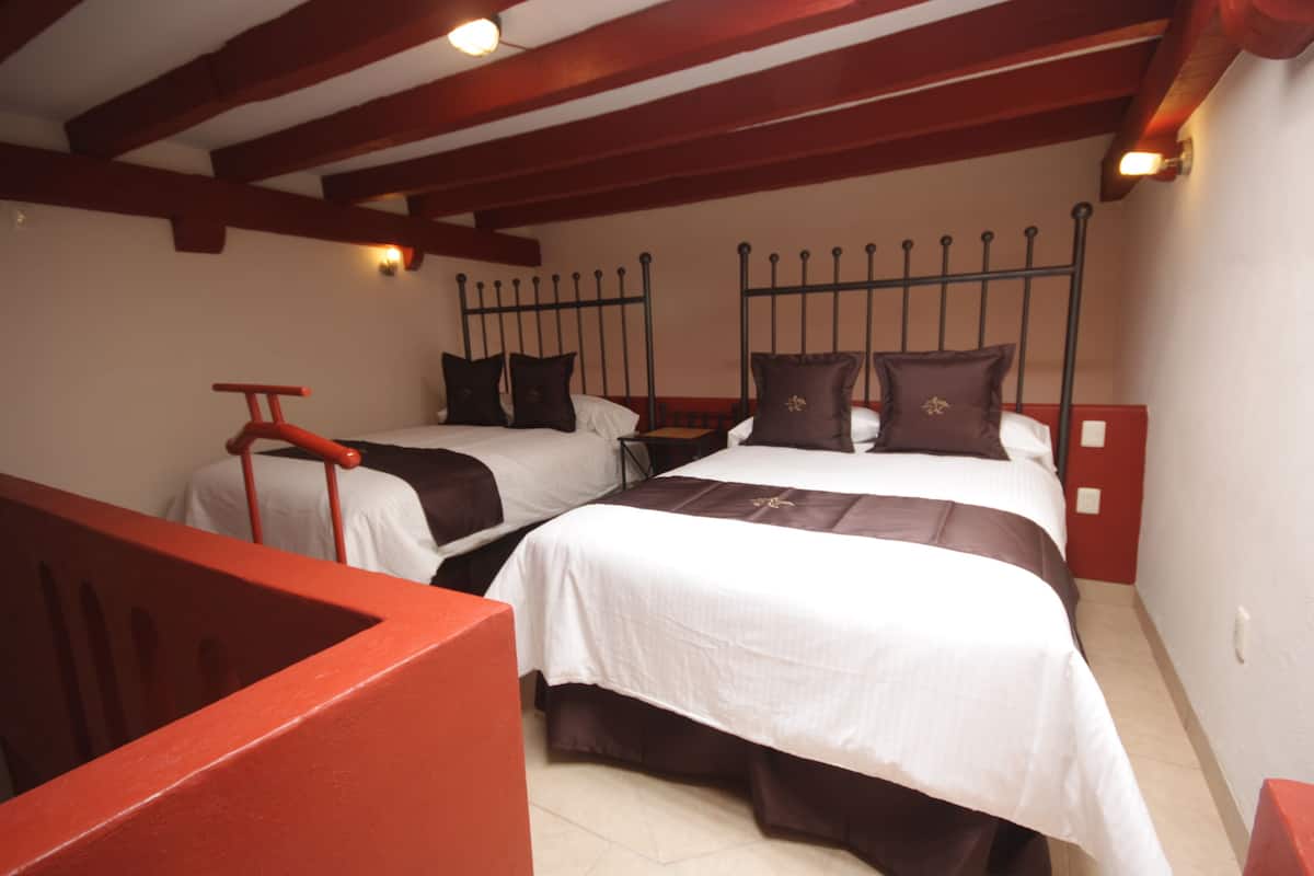 A room with two beds, wooden beams on the ceiling, and a red chair.