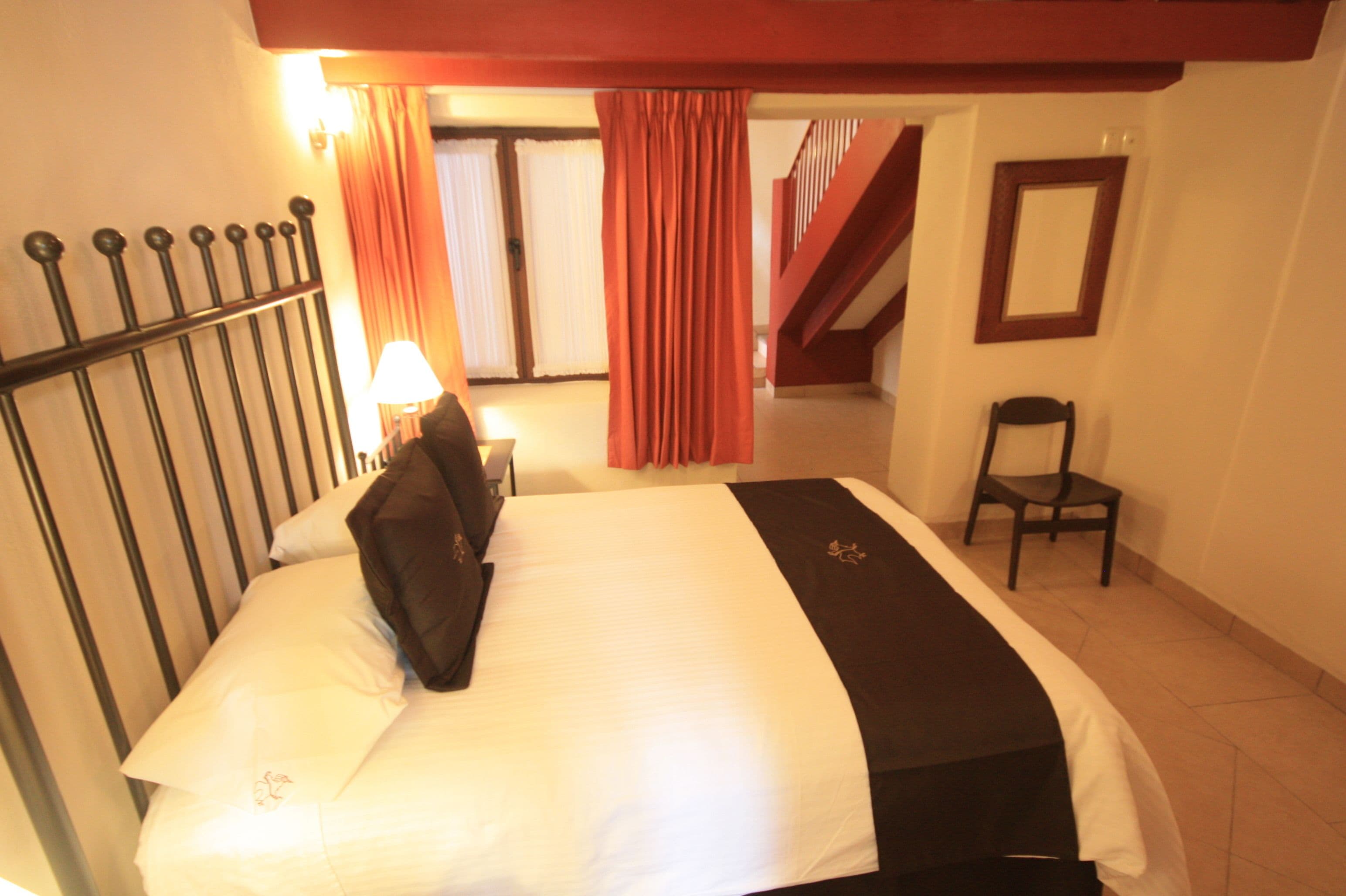 Una habitación de hotel con una cama, una silla, una lámpara y una escalera al fondo.