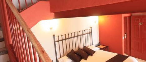 A bedroom with a bed, a wooden staircase, and a red wall with arched windows.