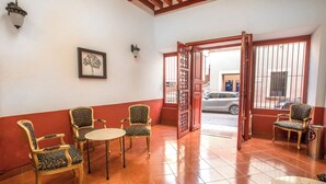 A hotel lobby with a red and white color scheme, a framed picture on the wall, and a view of the street through an open door. - Hotel Santa Regina (Guanajuato)