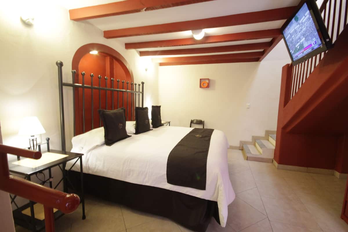 A hotel room with a bed, a desk, a chair, and a TV mounted on the wall.