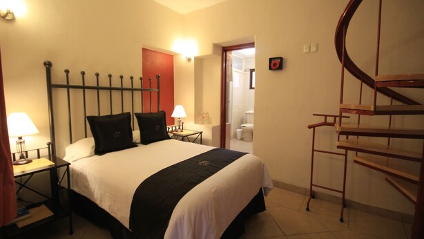 A hotel room with a bed, nightstands, a lamp, a red door, a bathroom, and a wooden spiral staircase. - Hotel Santa Regina (Guanajuato)
