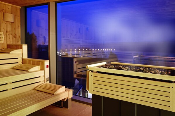 Una sala de sauna con bancos de madera y zona visible con puerta de cristal.