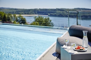 Un área junto a la piscina con una mesa para dos personas, que incluye una jarrón de vidrio, dos vasos y un plato con rebanadas de sandía.