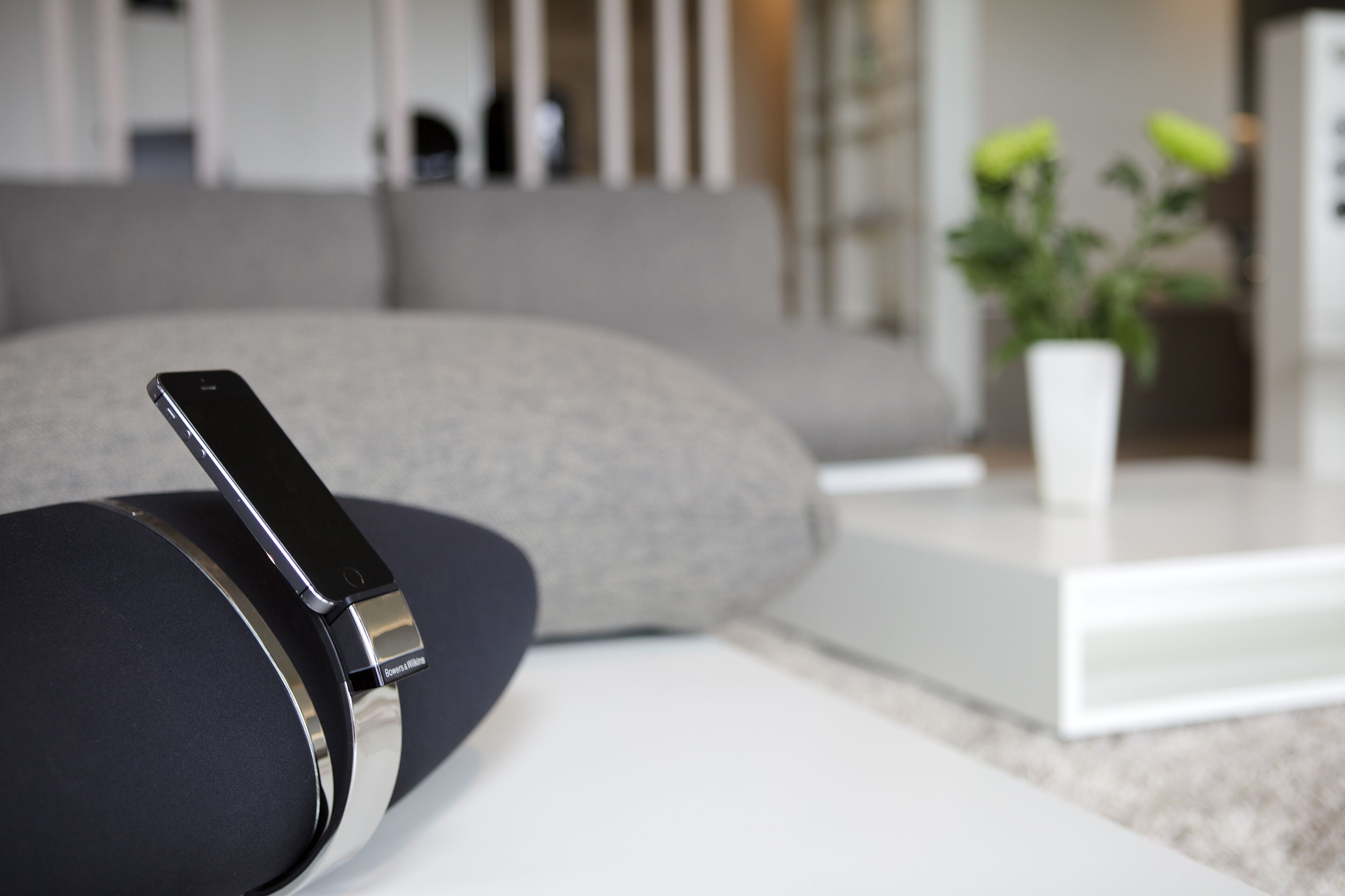 A modern living room with a sleek black and silver charging device on a white table, a grey sofa, and a white coffee table.