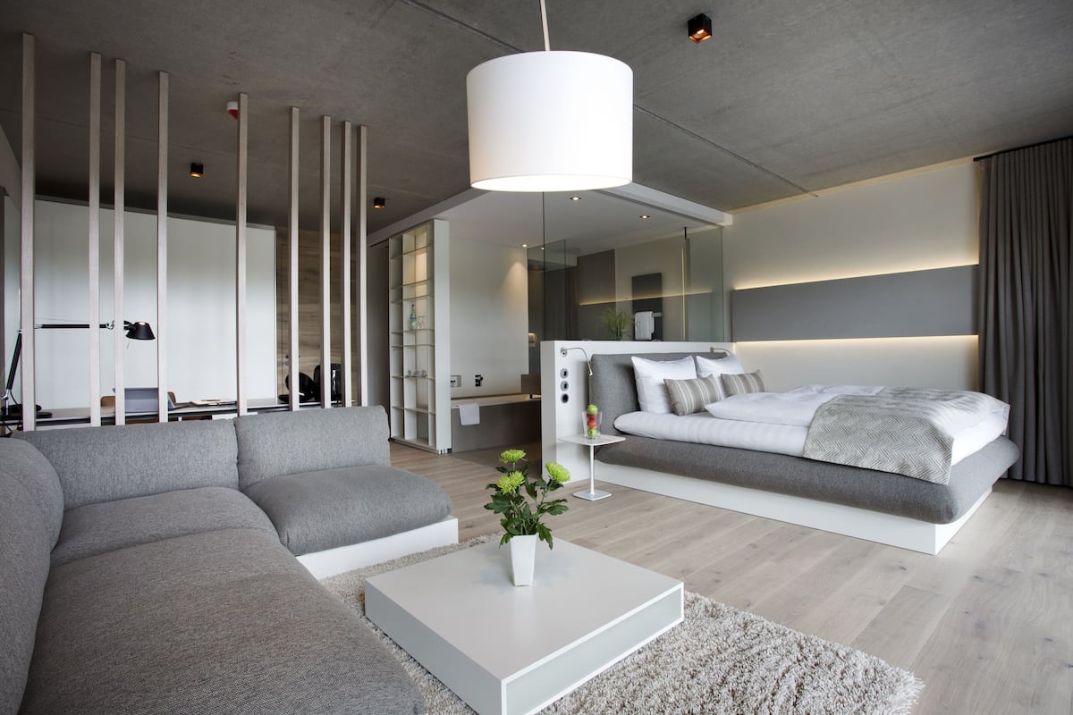 A modern living room with a sectional sofa, a white coffee table with a plant, and a large bed with a headboard.