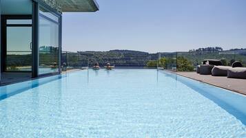 A modern infinity pool with clear blue water, surrounded by a glass enclosure and a wooden deck.