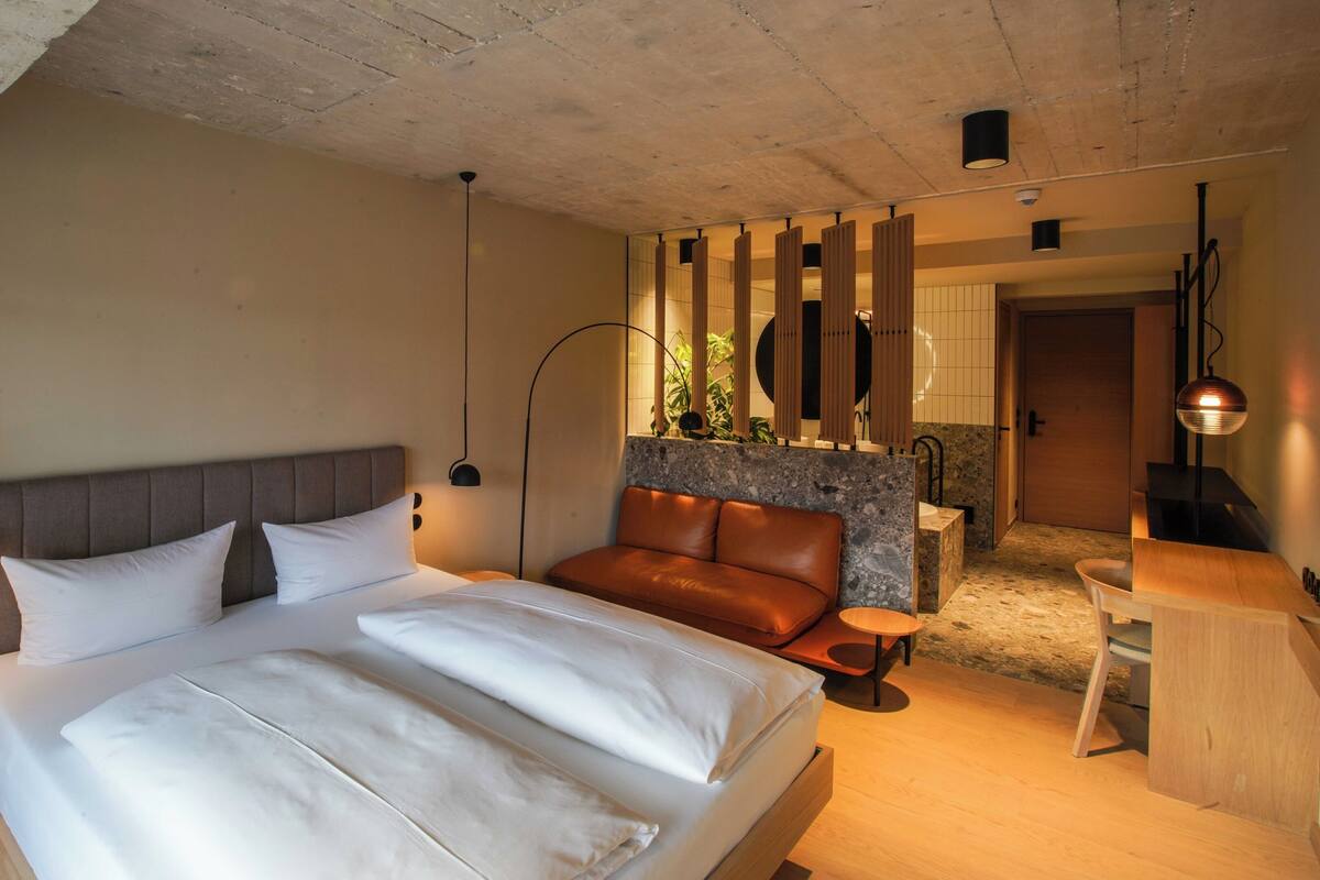 A modern bedroom with a large bed, a wooden headboard, a brown leather sofa, and a small wooden table.