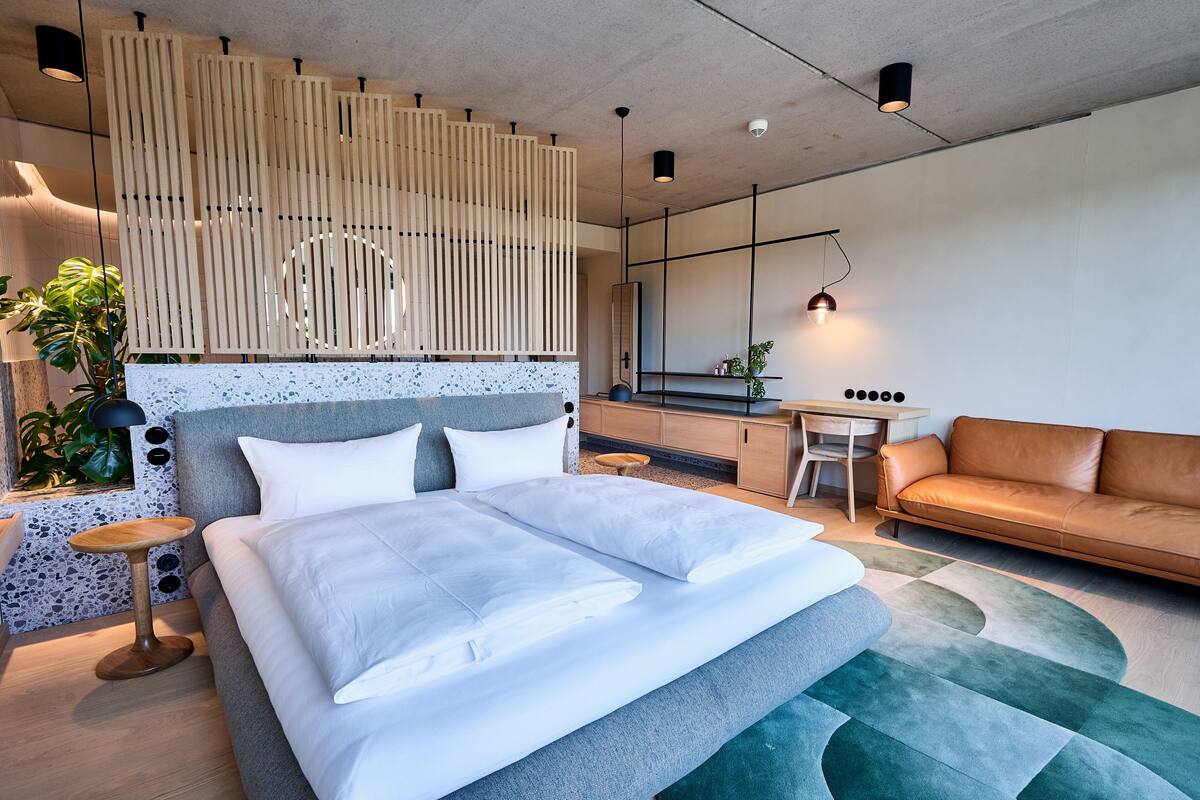 A modern bedroom with a large bed, a sofa, a desk, and a potted plant.