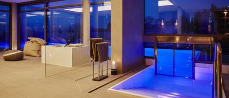 A modern hotel lobby with a large glass wall, a reception desk, and a seating area with a bench and a small table.