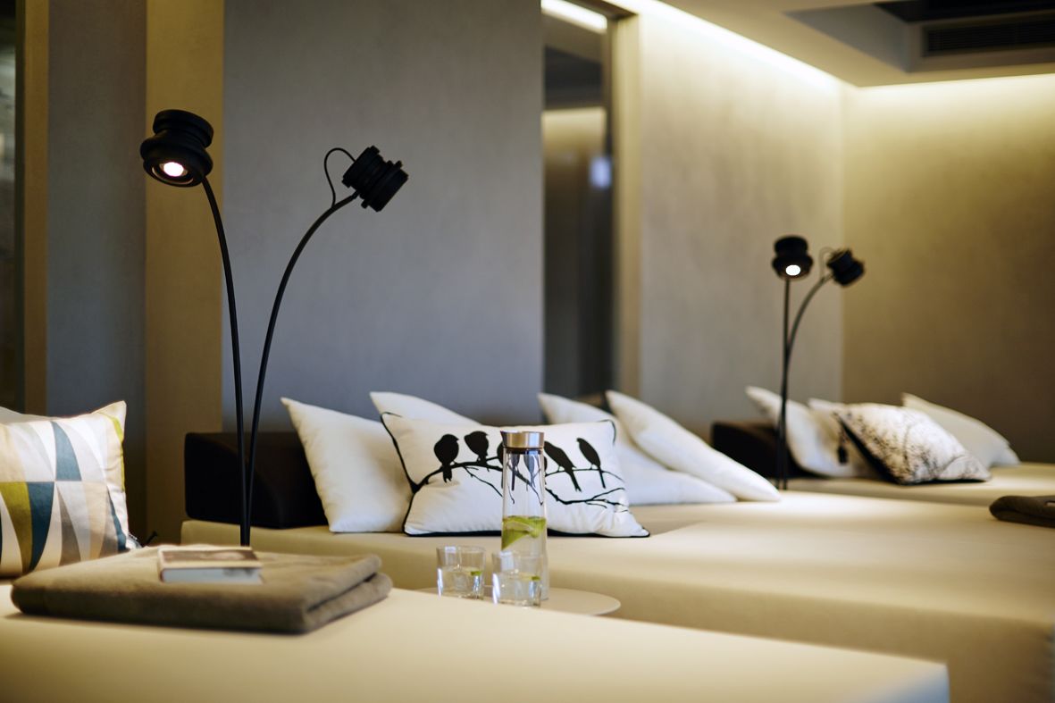 A modern hotel room with a bed, pillows, a bedside table, and two black floor lamps.