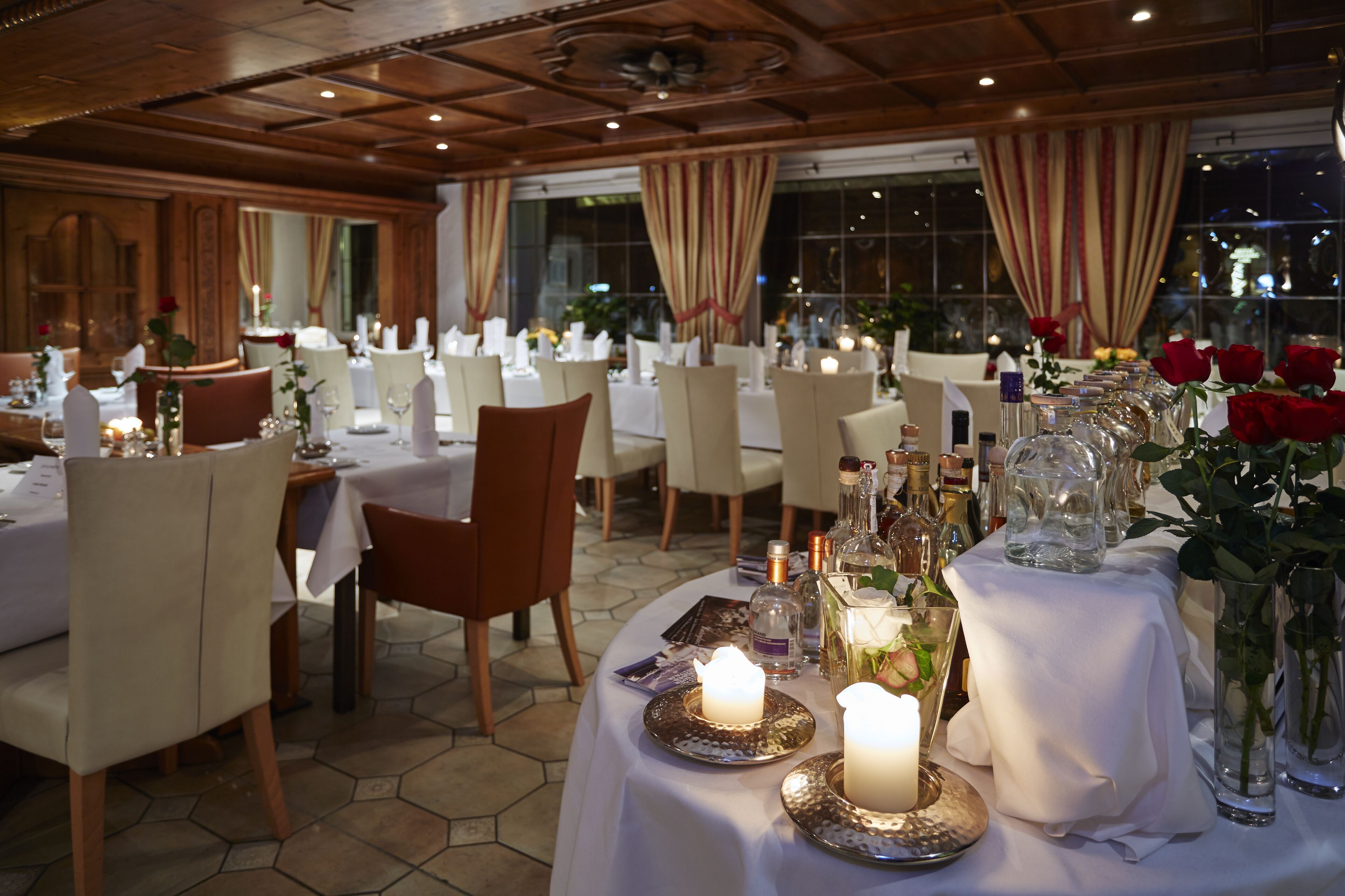 A restaurant with round tables covered in white tablecloths, candles, and red roses.