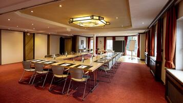 Un salón de conferencias con una larga mesa, sillas y una lámpara moderna.