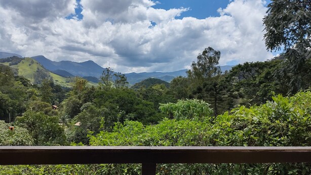 Un paysage luxuriant avec une balustrade en bois, une végétation dense et des montagnes lointaines sous un ciel partiellement nuageux.