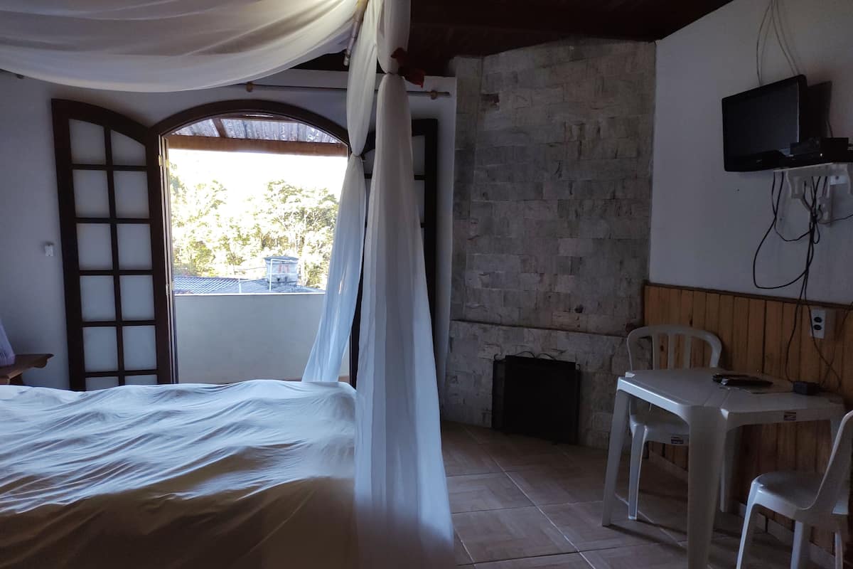 A room with a bed, a table, a chair, a television, and a view of the outside.