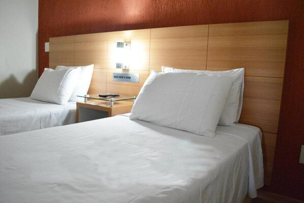 A hotel room with two single beds, wooden headboard, bedside tables, and a nightstand.