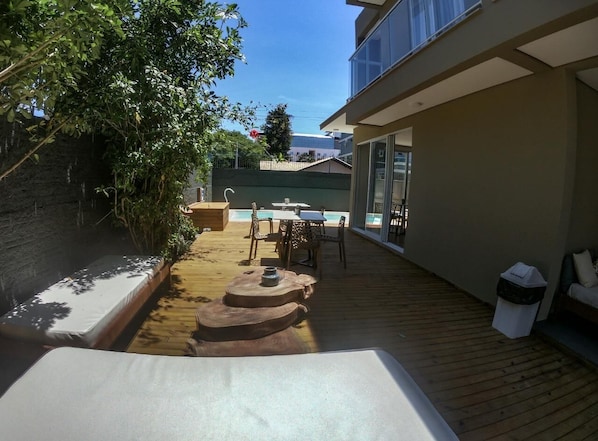 A poolside area with a wooden deck, a lounge chair, and a dining set.