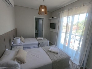 A hotel room with two beds, a television, a window with curtains, and a ceiling fan.