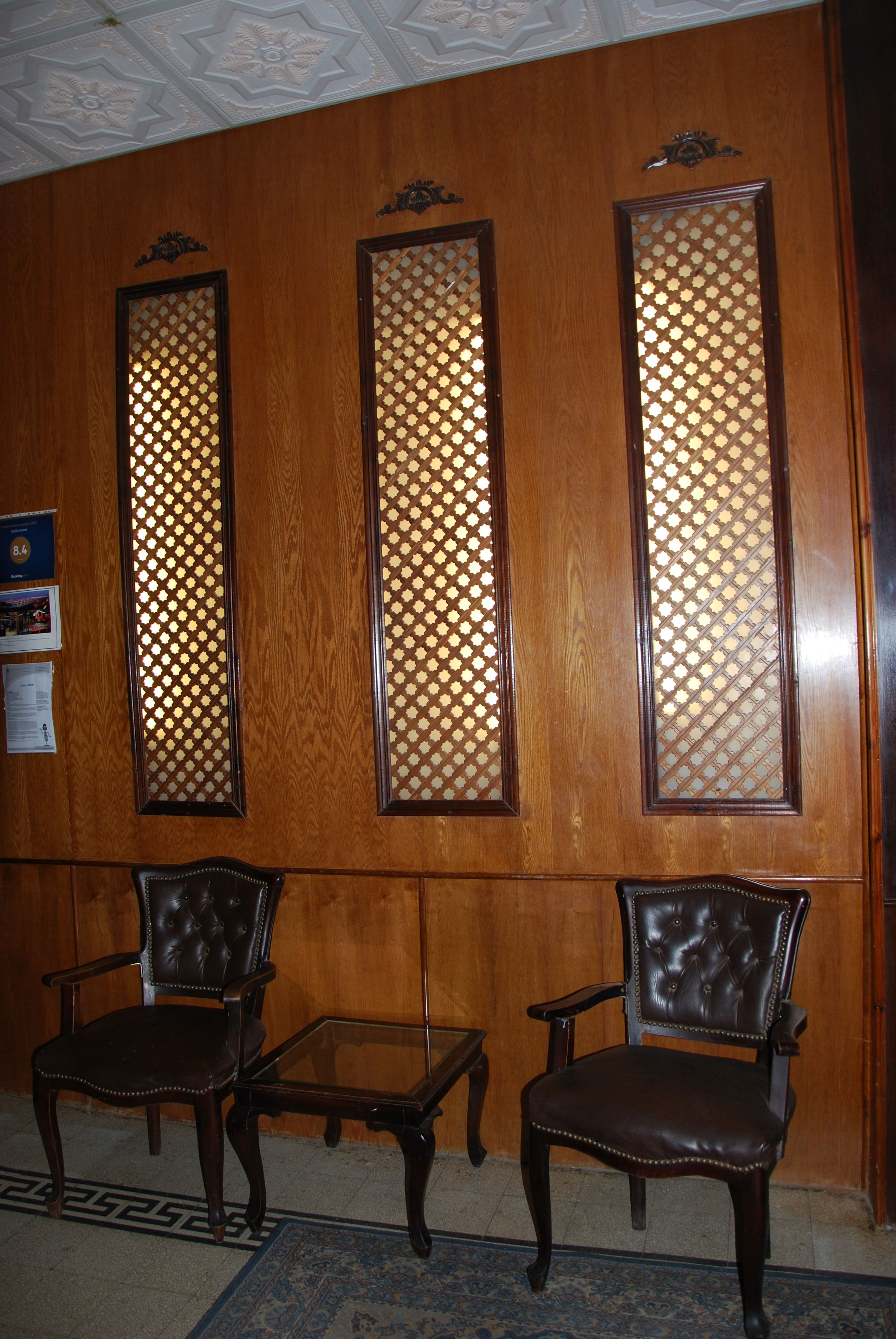 Une pièce avec trois panneaux de bois ornés de motifs en treillis, deux fauteuils en cuir et une petite table en verre.