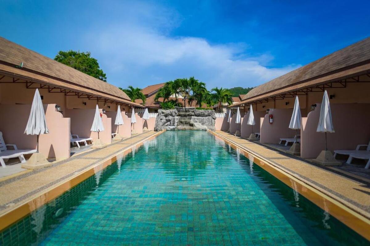 Una piscina con sillones de descanso y sombrillas, rodeada de edificios de diseño tropical.