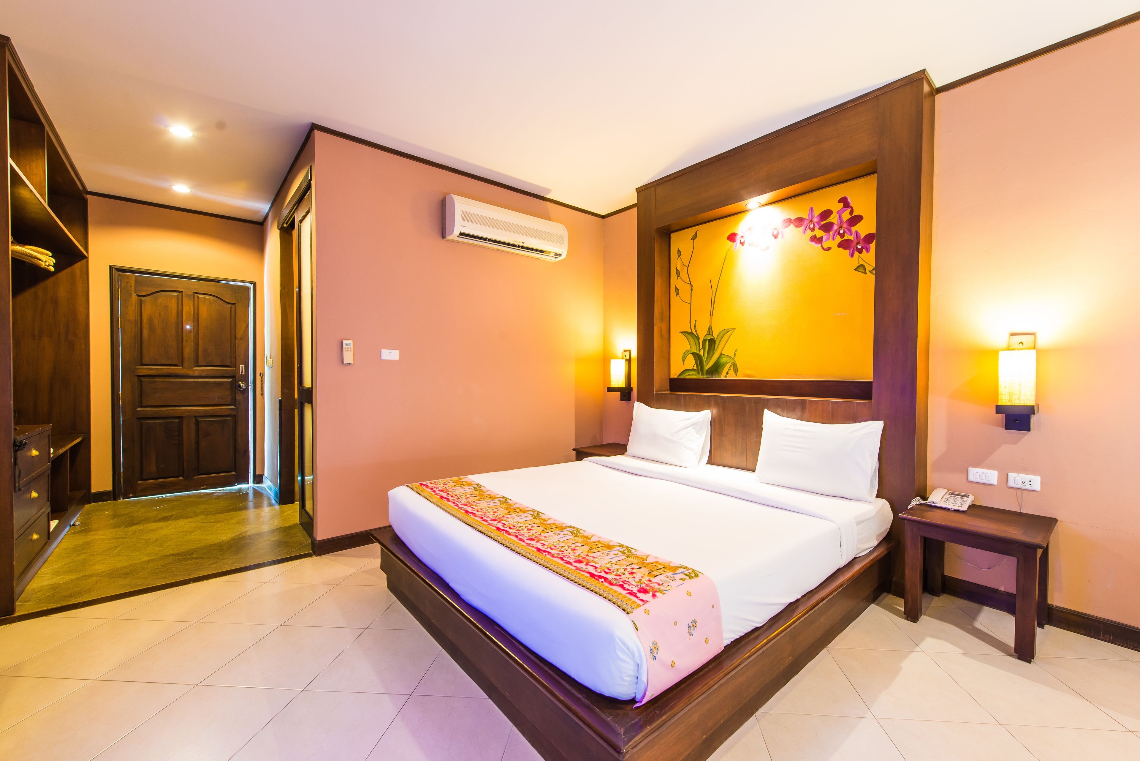 Quarto de hotel com uma cama grande, cabeceira de madeira, mesa de cabeceira com telefone e ar condicionado na parede.