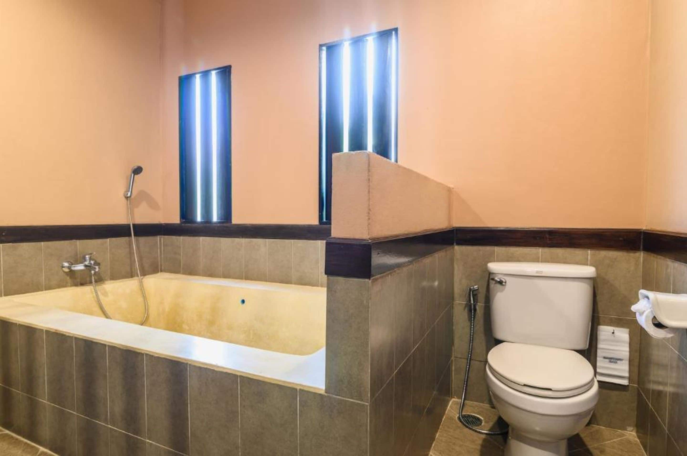 A bathroom with a bathtub, toilet, and two windows with blinds.