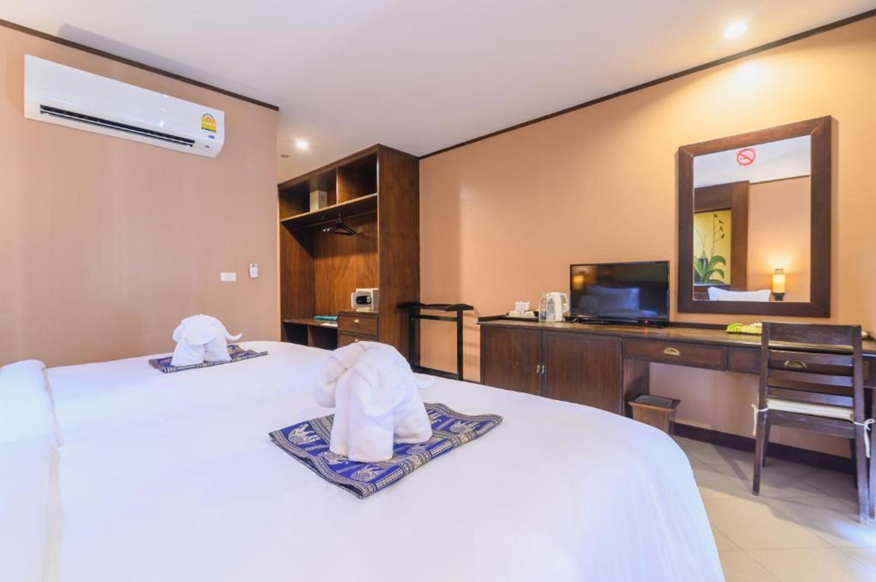 A hotel room with two beds, a desk, a TV, a wardrobe, and an air conditioning unit.