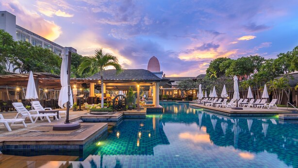 A pool area with lounge chairs and umbrellas, surrounded by buildings and palm trees.