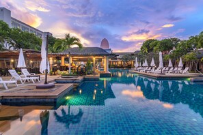 A pool area with lounge chairs and umbrellas, surrounded by buildings and palm trees.