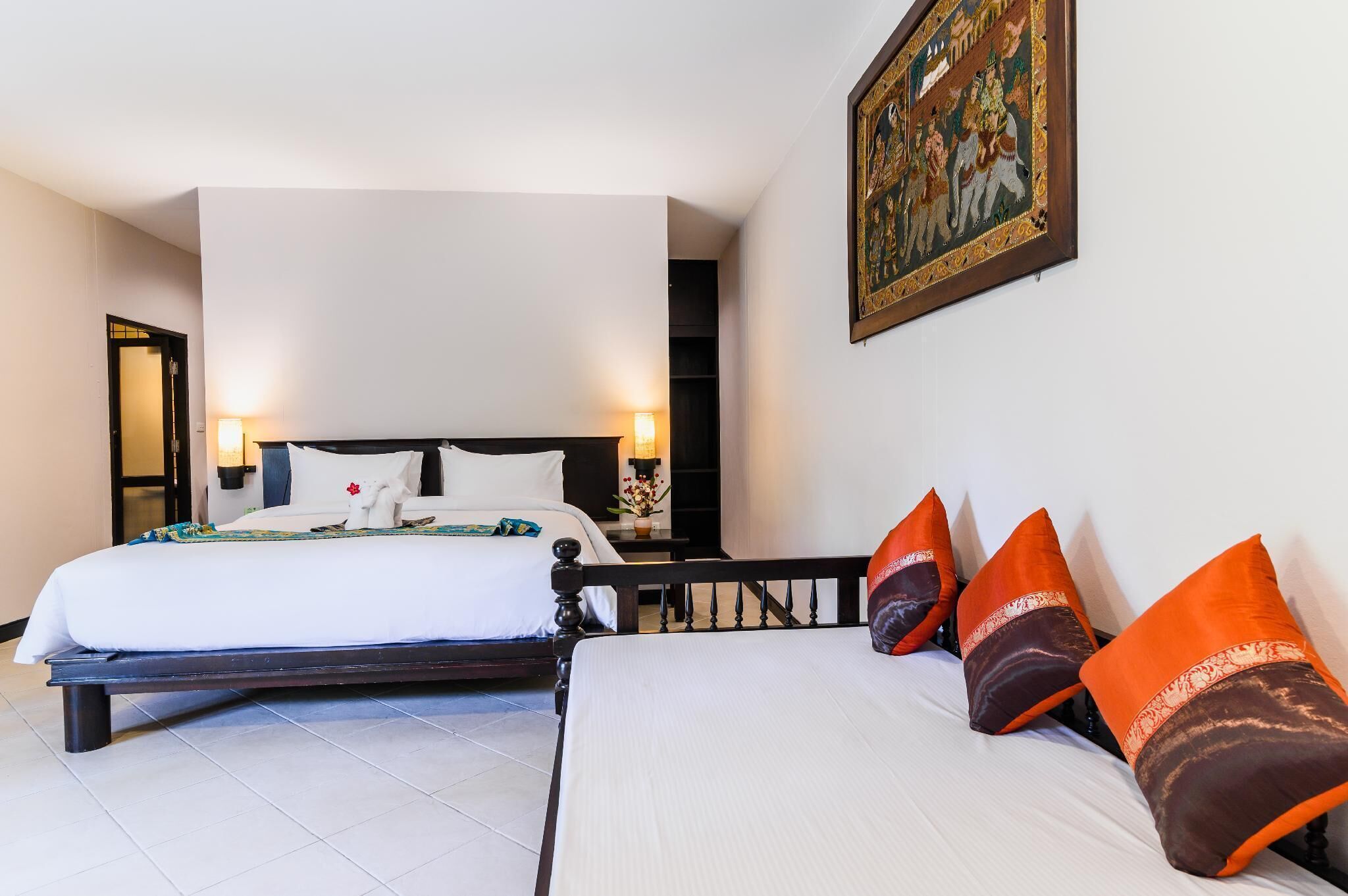 Una habitación de hotel con una cama grande, una cama más pequeña y una mesita de noche con lámpara.