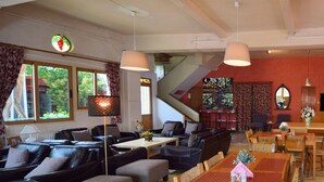 A dining area with long wooden tables, cushioned seating, and pendant lighting.