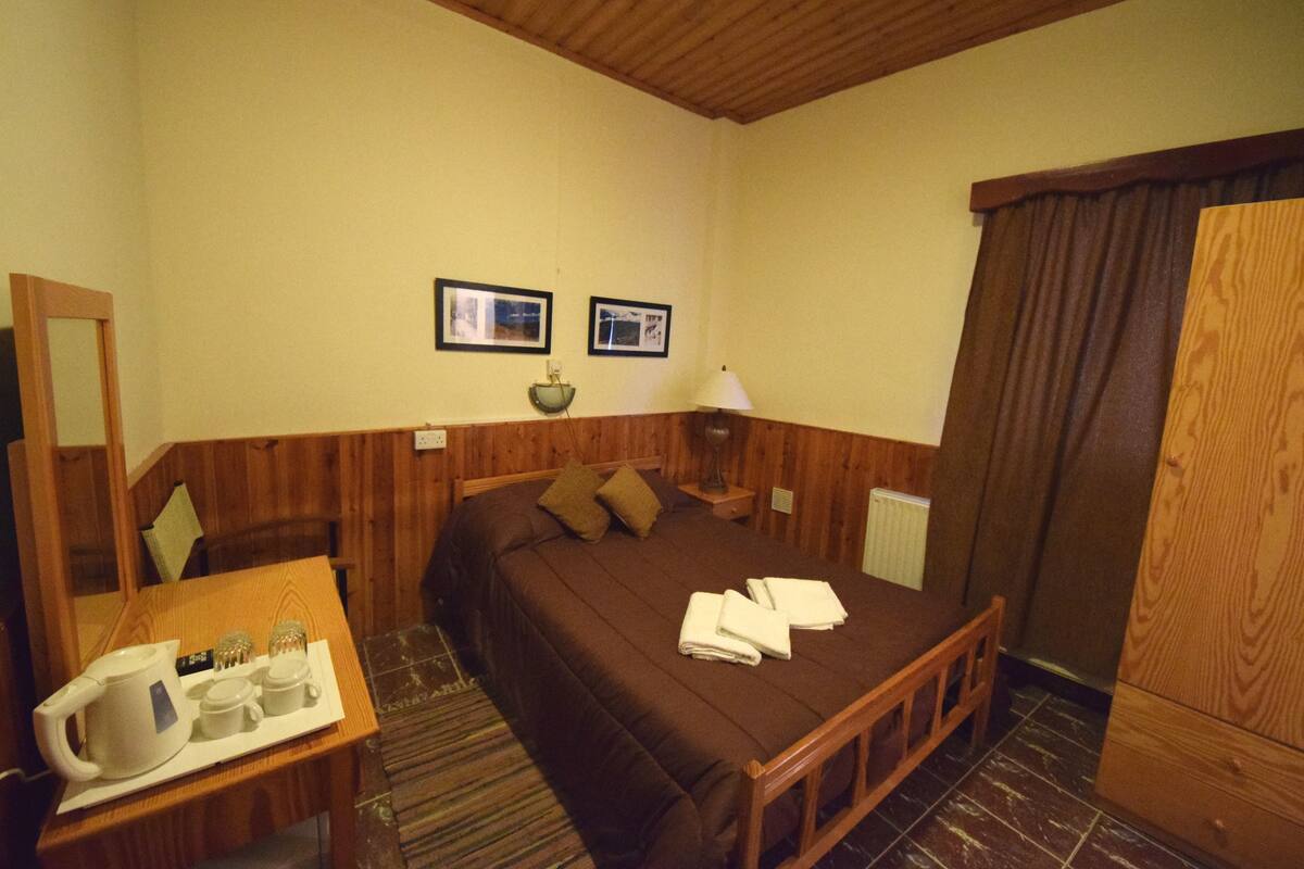 Een slaapkamer met een houten bed, een nachtkastje met een lamp, een spiegel en twee ingelijste foto's aan de muur.