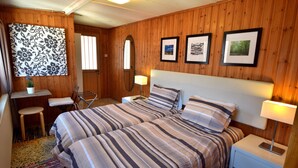 A room with wooden paneling, a bed with striped bedding, a desk with a chair, a mirror, and framed pictures on the wall.