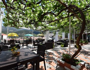 Un patio al aire libre con mesas, sillas, sombrillas y plantas en macetas.