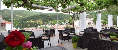 An outdoor seating area with tables and chairs, a potted plant, and a vase with flowers.