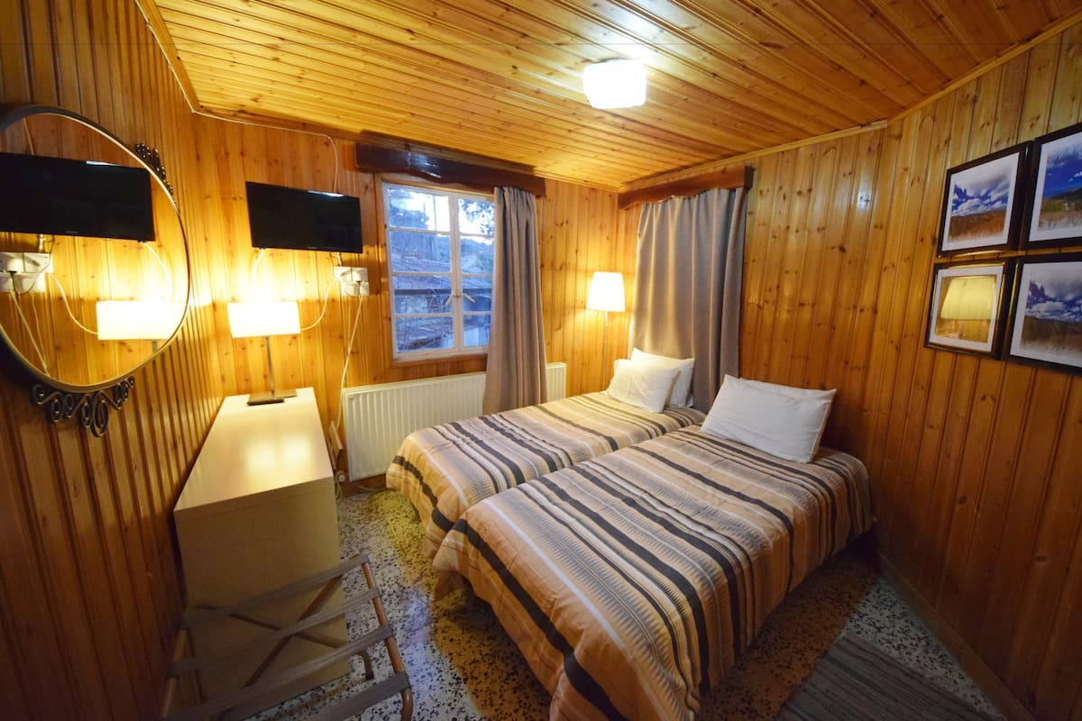 Een kamer met houten lambrisering, twee bedden, een bureau en een raam.