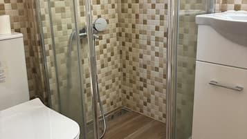 A bathroom with a glass-enclosed shower, a toilet, and a sink.