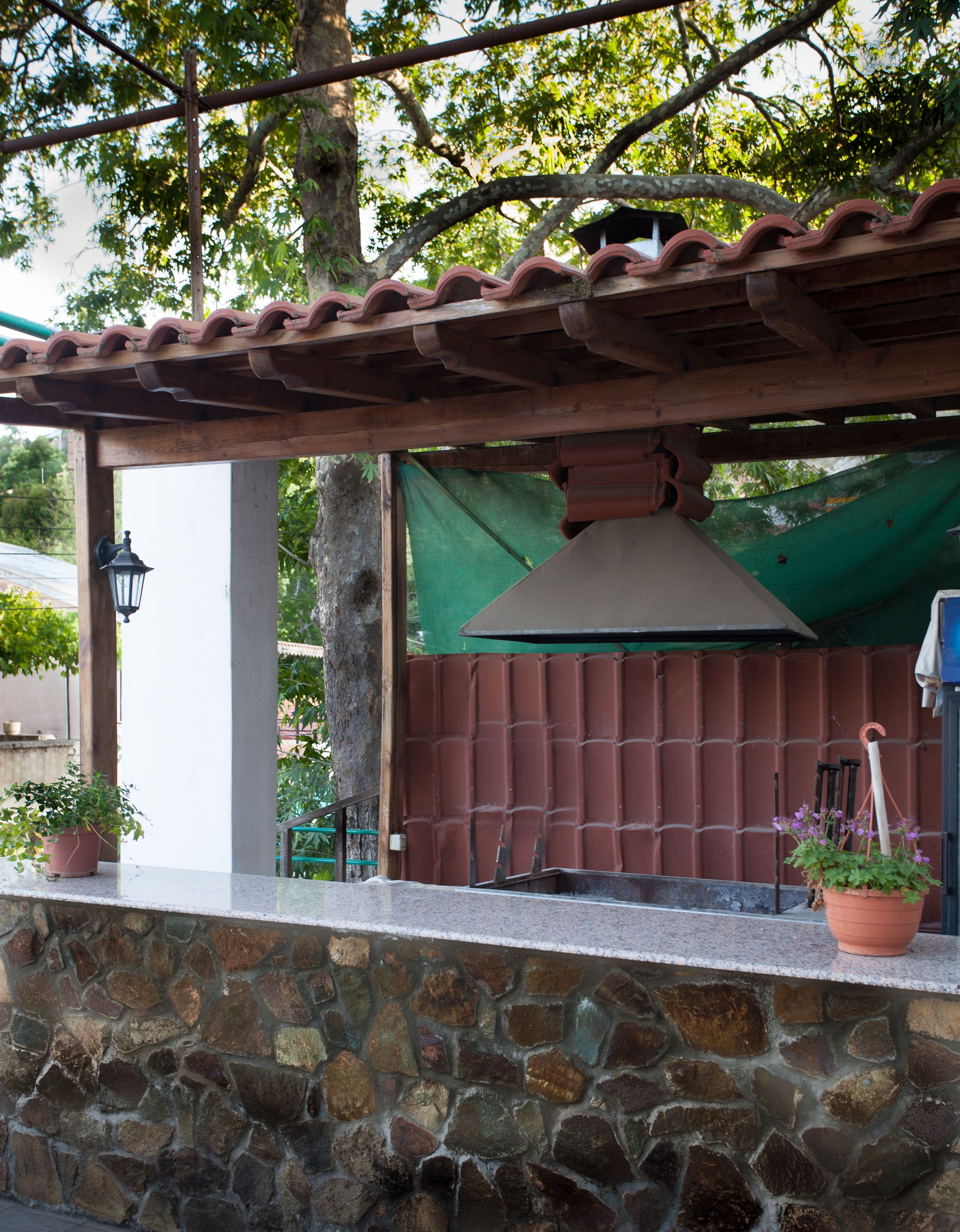 A stone wall with a tiled roof structure, a green tarp, and a potted plant.