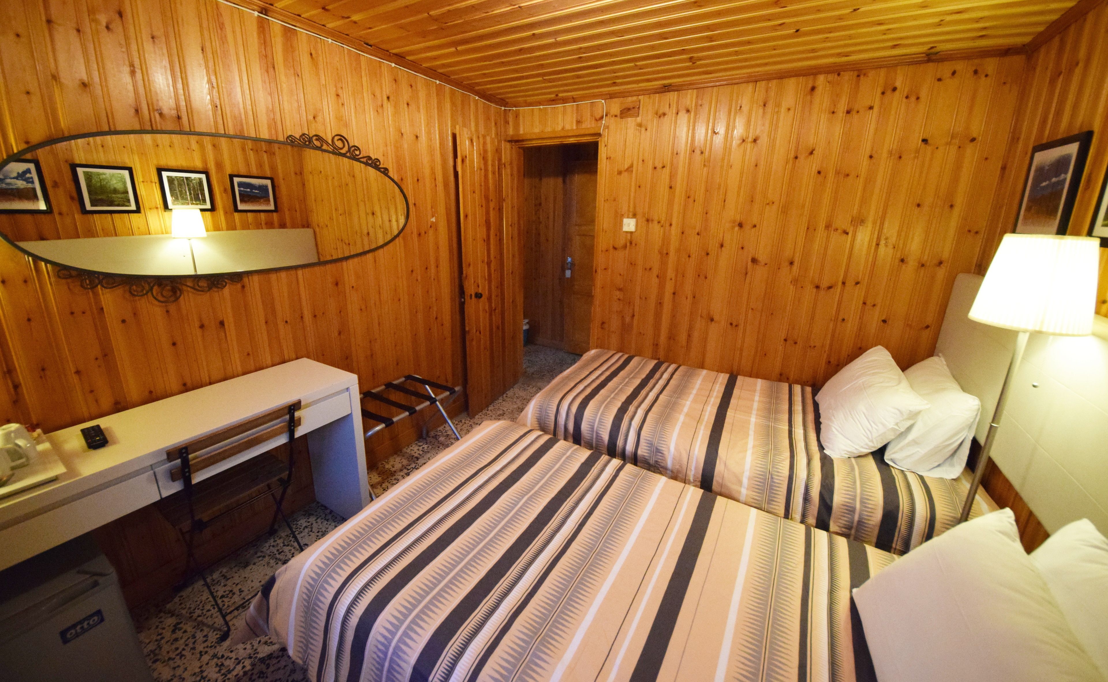 A wooden-paneled room with two beds, a desk, and a mirror.