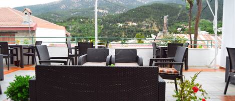 Terraço com mobiliário de vime e plantas em vasos, com vista para uma paisagem montanhosa.
