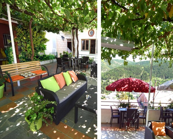 A patio with a sofa, chairs, and a table, surrounded by potted plants and a view of a mountainous landscape.