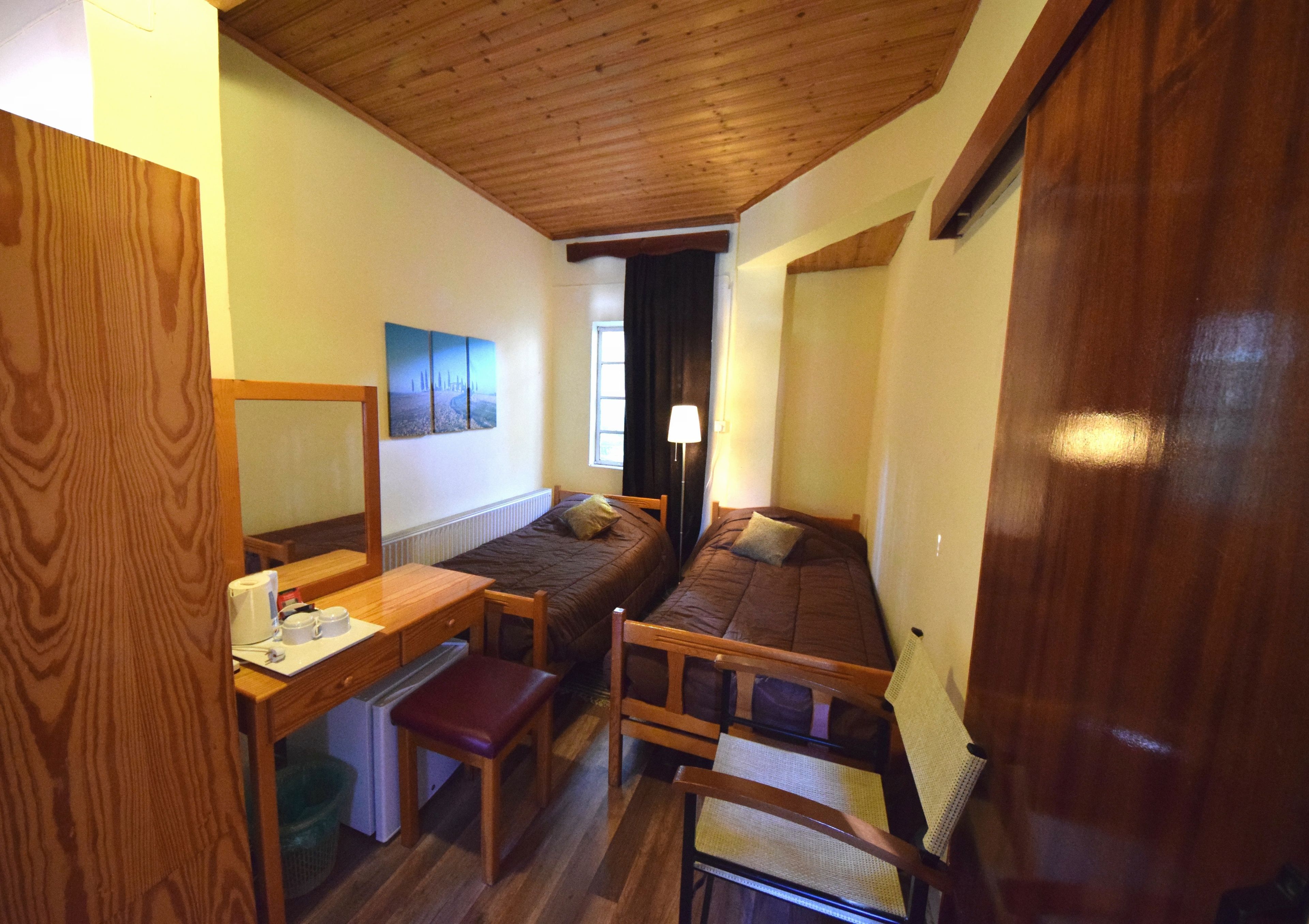 A compact bedroom with a single bed, a desk with a chair, a small table, and a mirror.