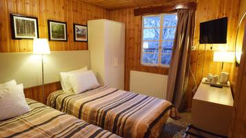 A room with two beds, a wardrobe, a window with curtains, a television, and a small table with a lamp.