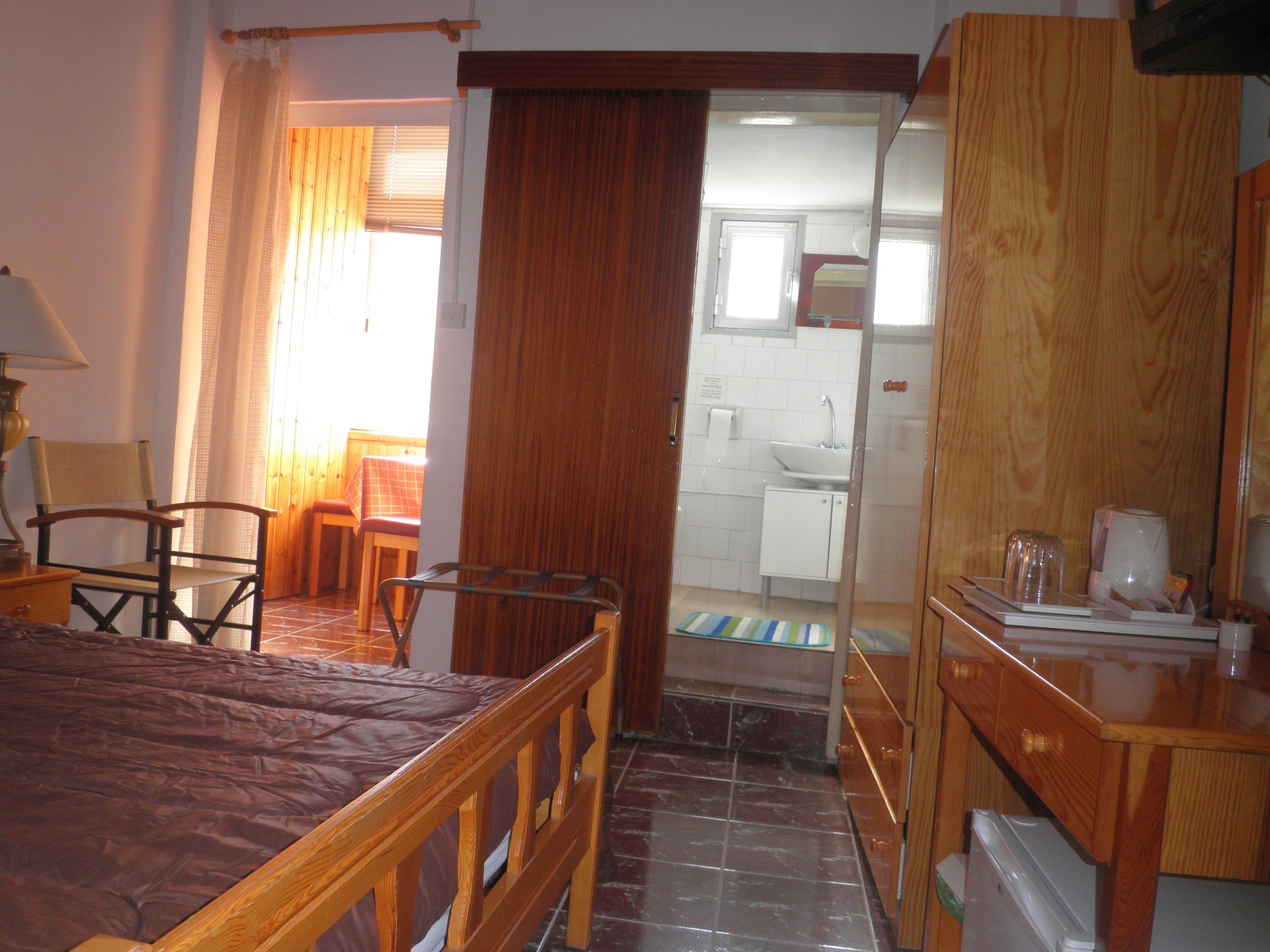 Een hotelkamer met een bed, een bureau, een stoel, een klein tafeltje en een badkamer die door een open deur zichtbaar is.