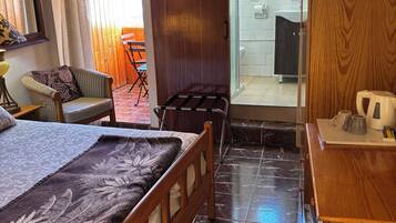 Habitación de hotel con cama, escritorio de madera, silla, una mesita y baño visible a través de una puerta abierta.
